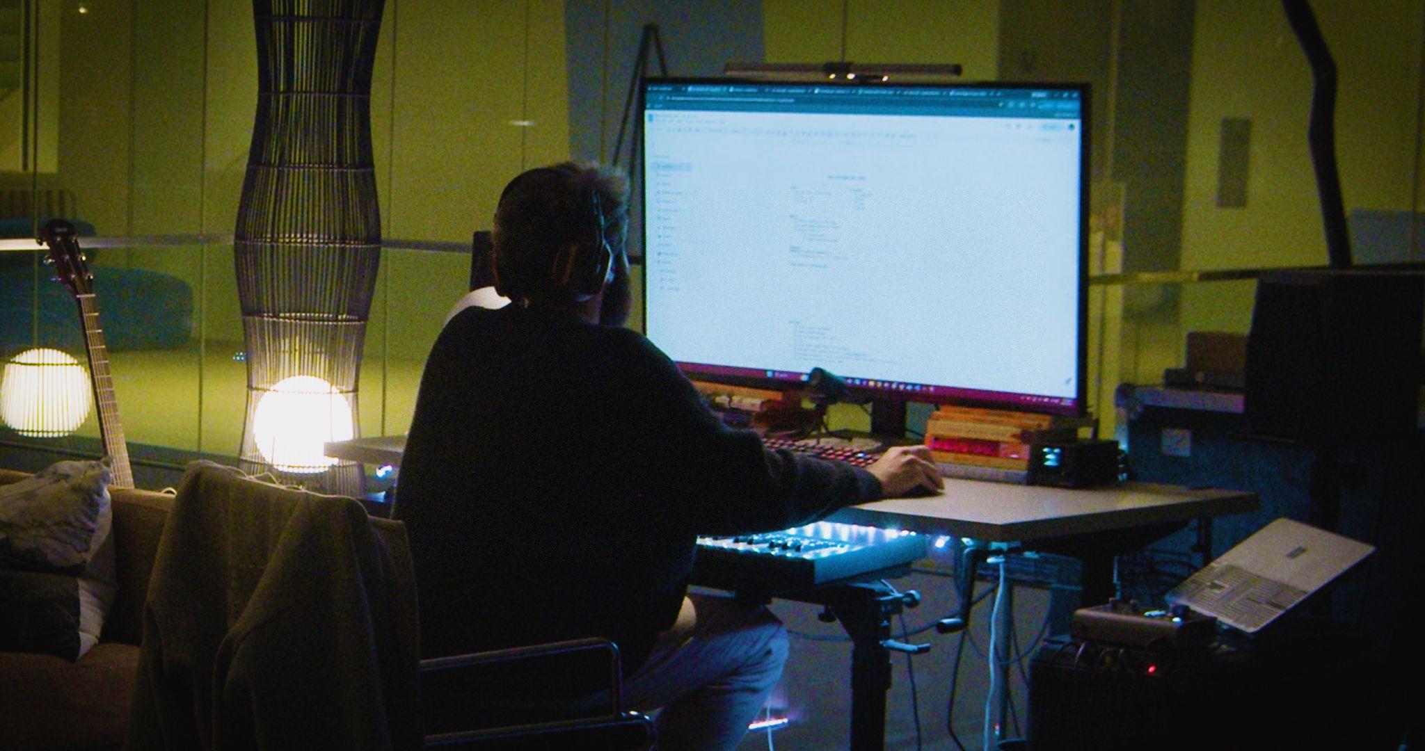 Vid. 05 — A man wearing headphones, staring at a larger computer monitor | Link: